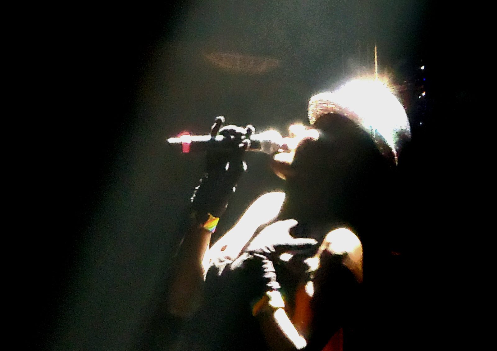 A performer on stage, lit from above by a spotlight, raising a microphone to her mouth in one hand clutching her chest in the other.